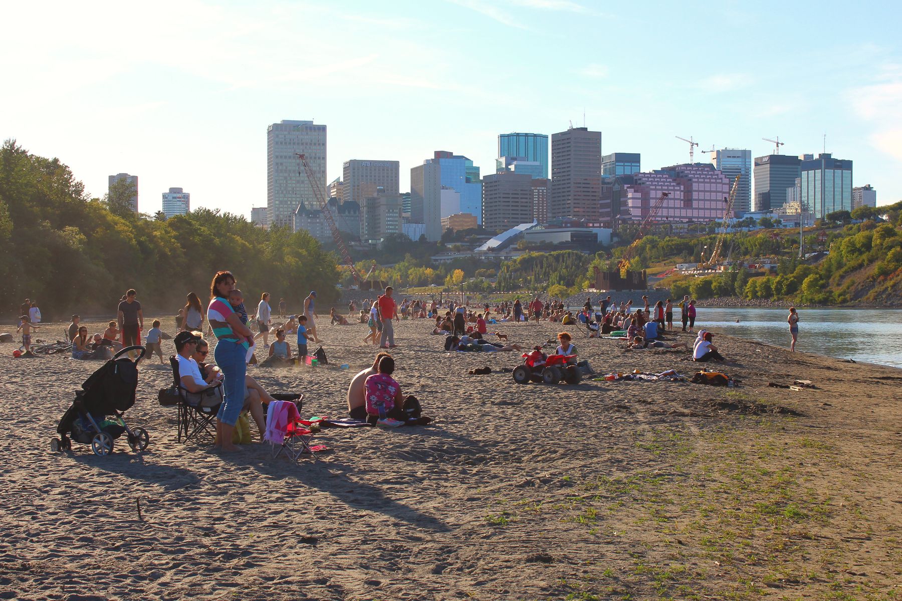 Families on the sand at Accidental Beach with the Edmonton skyline across the North Saskatchewan River