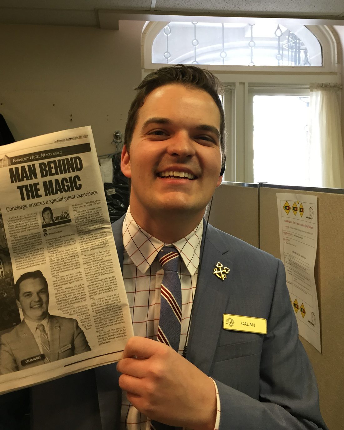 Calan Hobbs at the concierge desk of the Fairmont Hotel Macdonald, holding a newspaper profile of his work headlined Man Behind the Magic