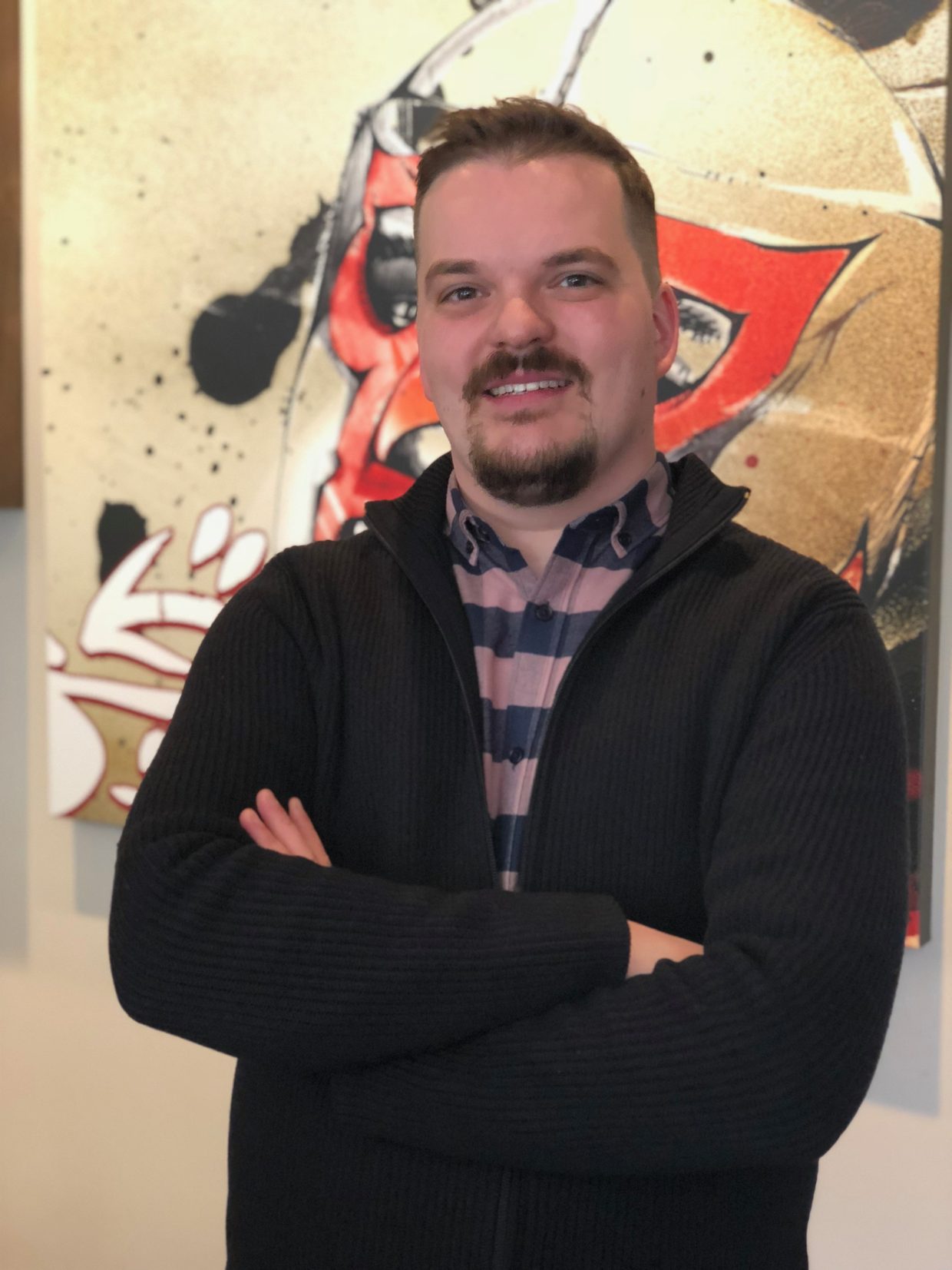 Calan Hobbs standing with his arms folded in front of a large painting
