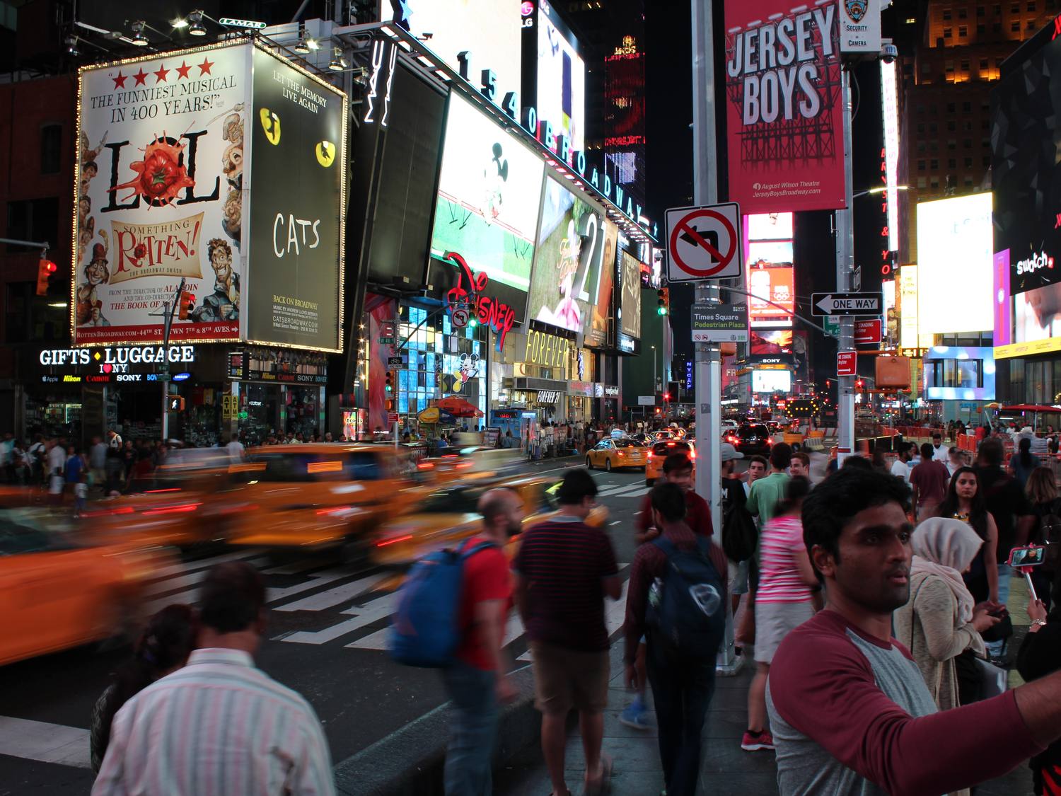 Stacked billboards and screens above the crowd and a motion-blurred taxi in Times Square, New York. Website design and management, Edmonton
